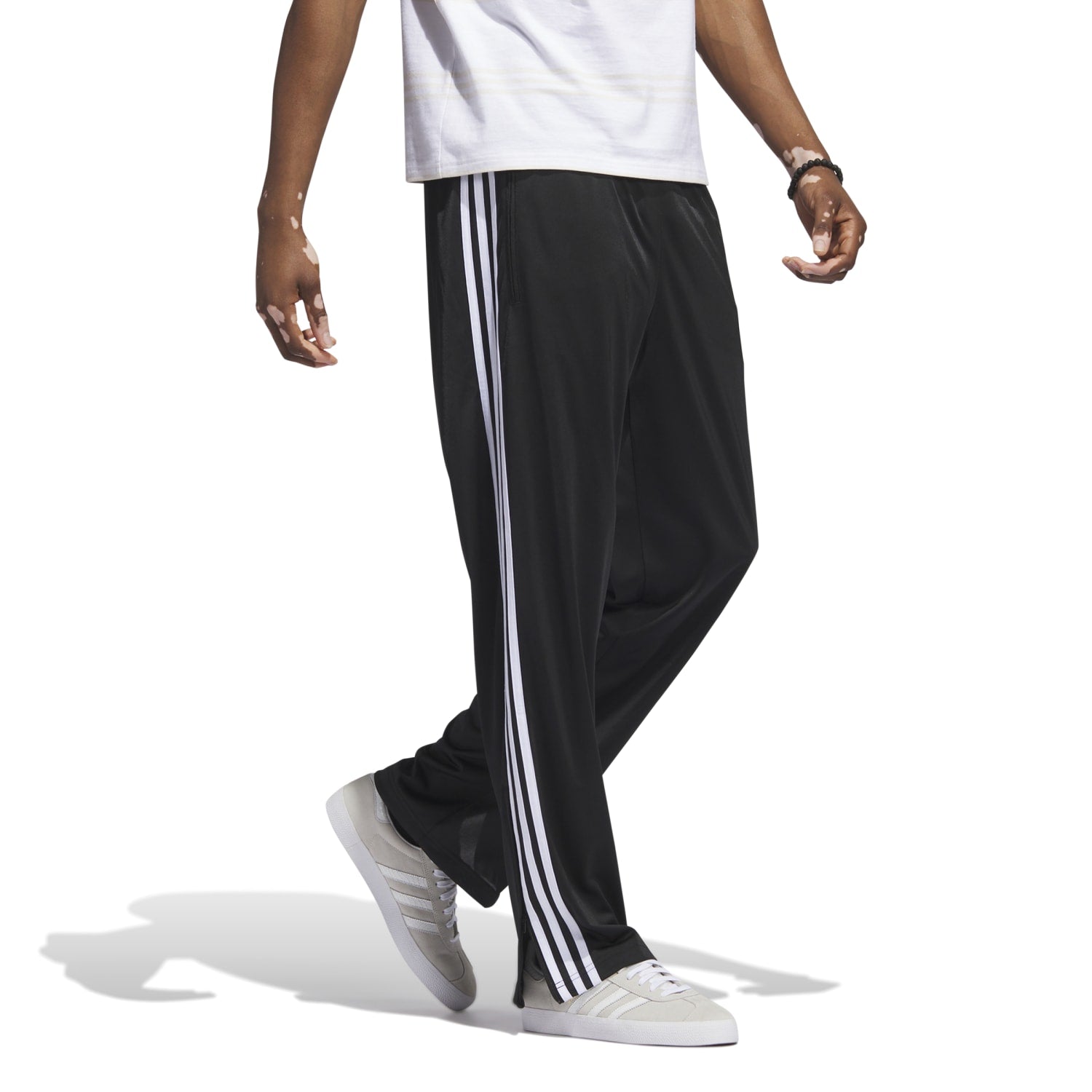 Side angle of runner tying shoes while wearing the best mens track pants for running—note the relaxed fit and trefoil logo