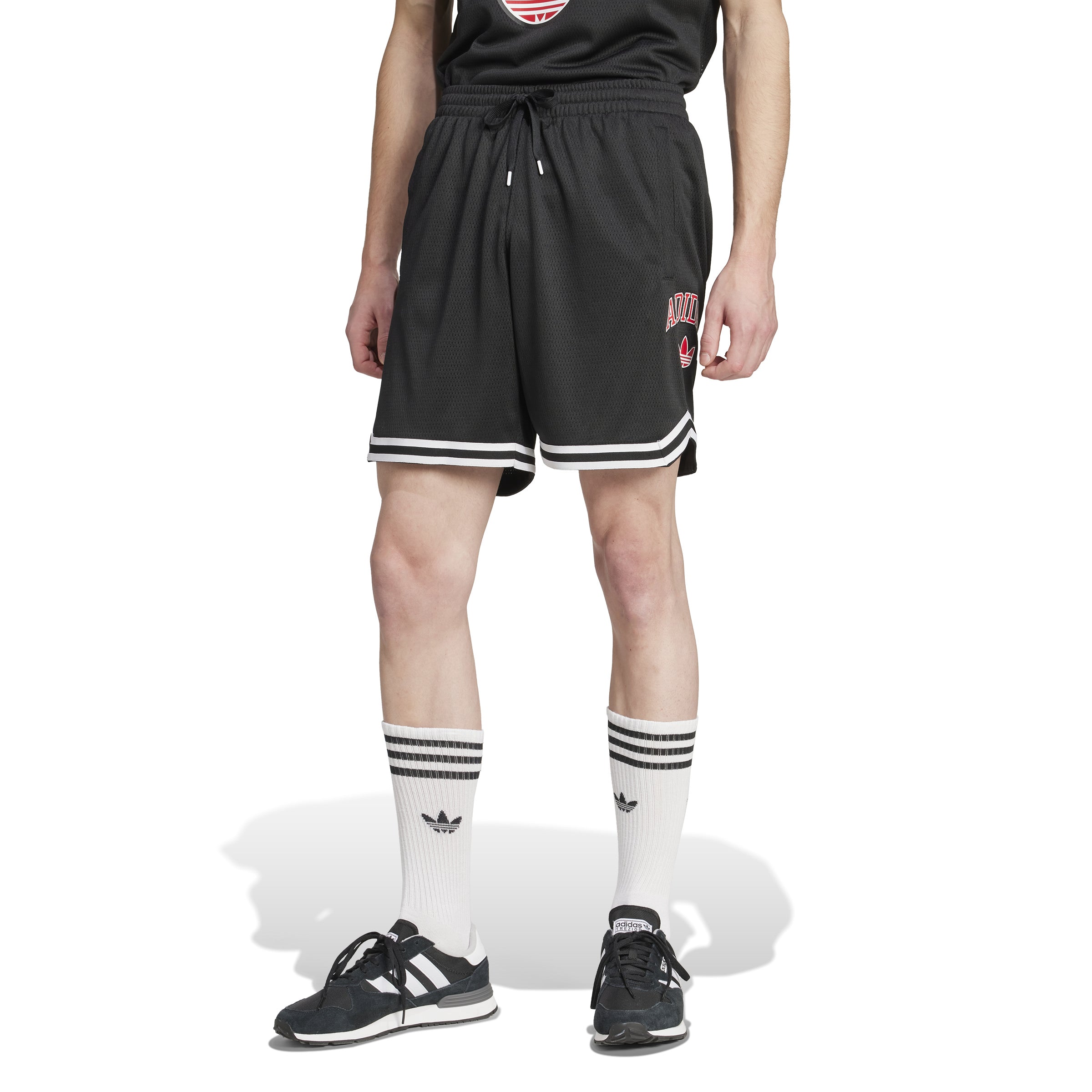 Male athlete in varsity sportswear performing a jump shot in basketball shorts