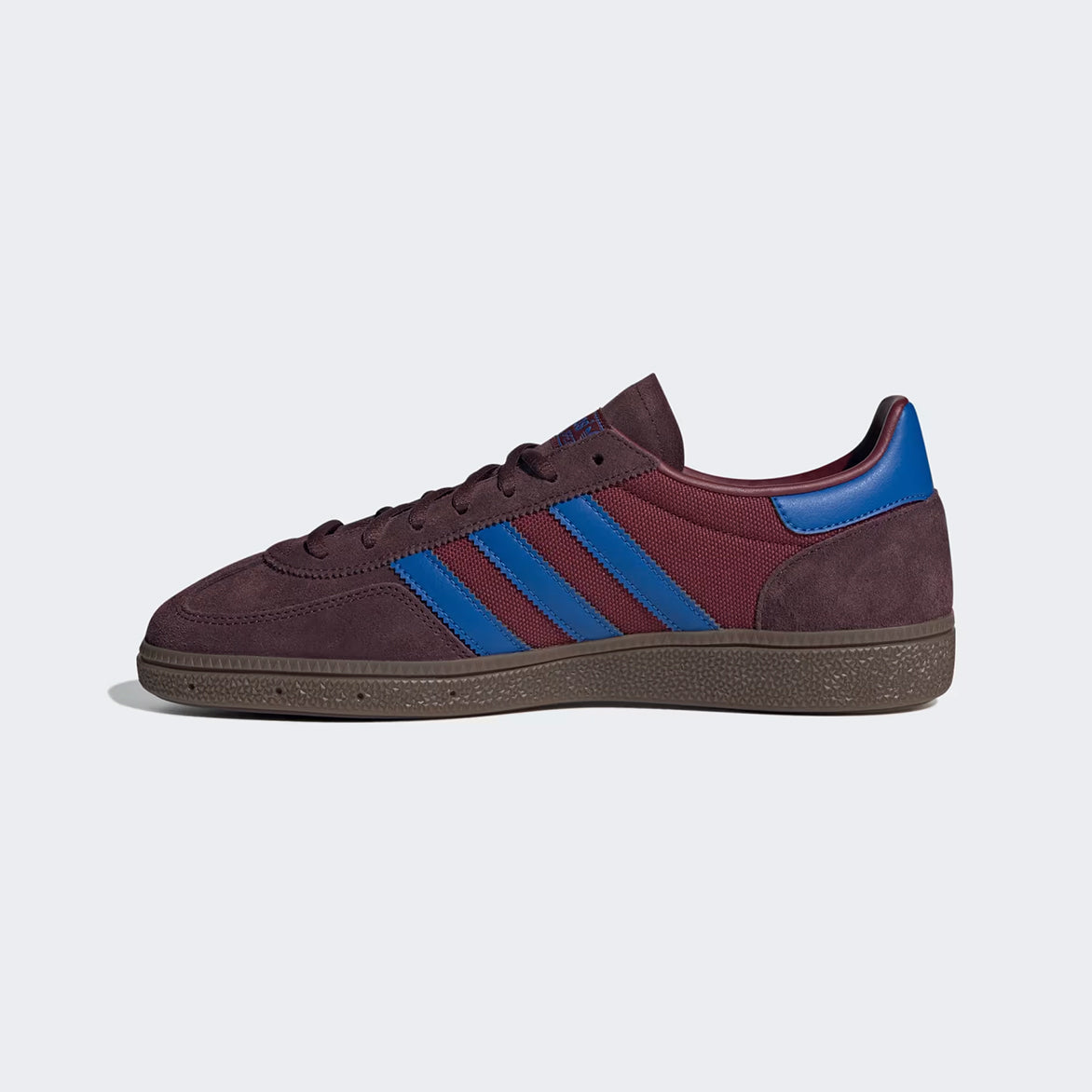 Side view of limited edition Adidas Handball Spezial Night Red sneakers on a casual outdoor setting.