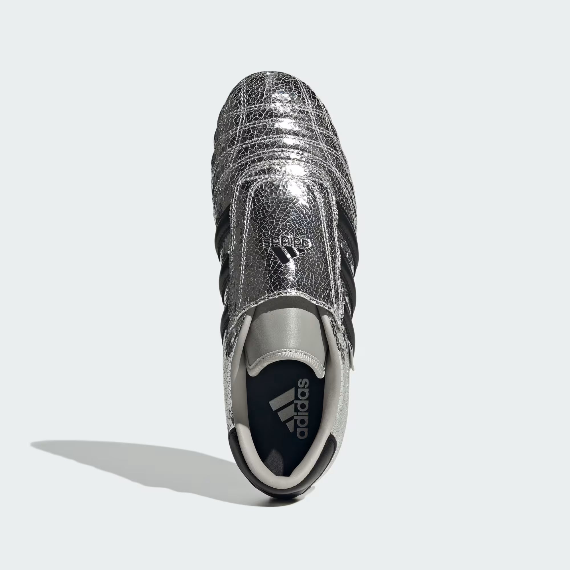 Close-up of silver metallic slip-on sneakers showing cracked leather texture and Trefoil logo