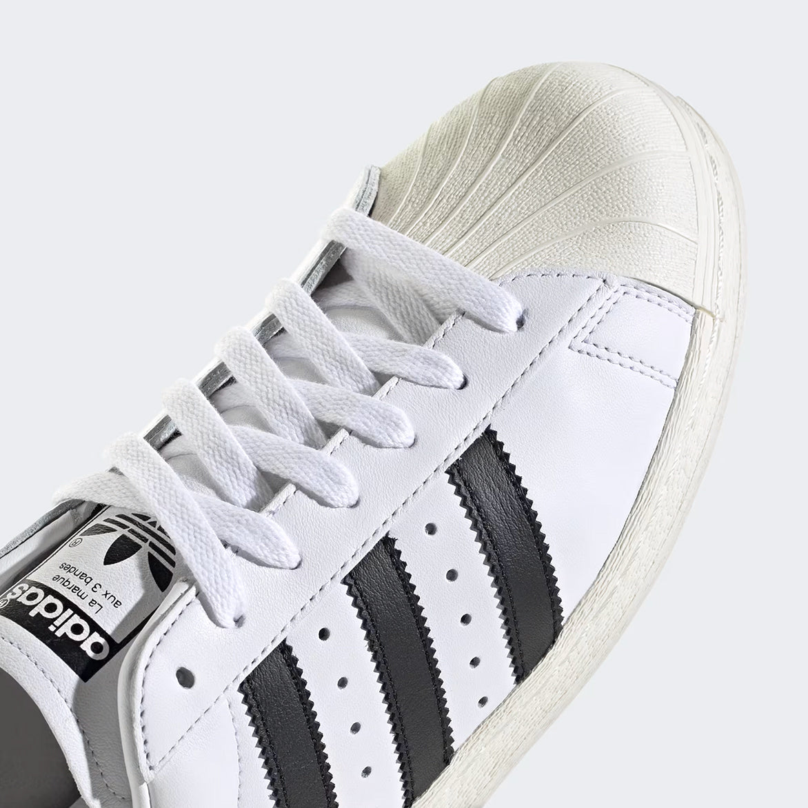 Side view of Adidas Superstar 82 showcasing the white leather upper and black detailing.