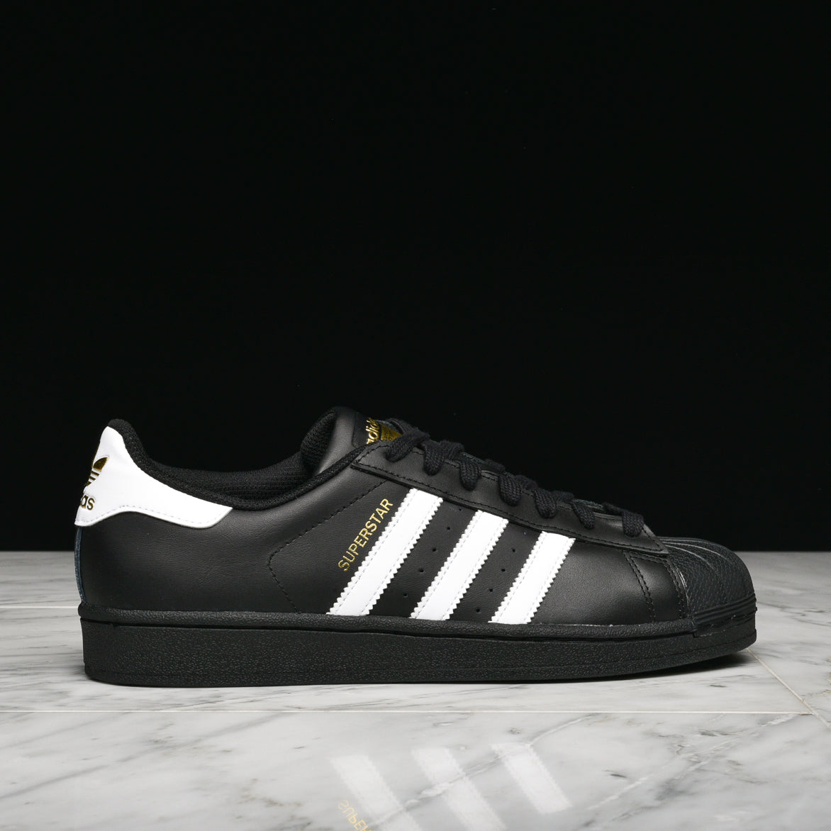Adidas Superstar sneakers in black and white, highlighting the rubber shell toe and leather upper.