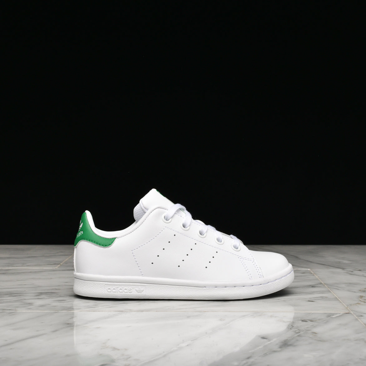 Close-up of Adidas Stan Smith sneakers showcasing the white leather and green accents for kids.